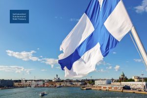 Hulmuava Suomen lippu, jonka taustalla näkyy Helsinki mereltä kuvattuna.