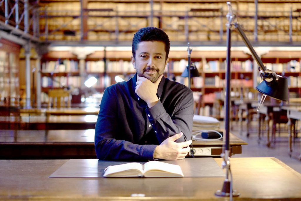 In the photo, architect Anis Souissi sits at a table in the National Archives of Finland’s reading room and looks toward the camera.