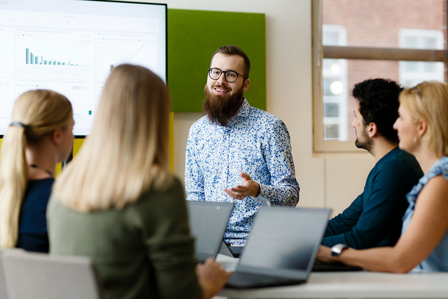 Nuori mies esittelee tilastoja pöydän ääressä istuville kollegoilleen.